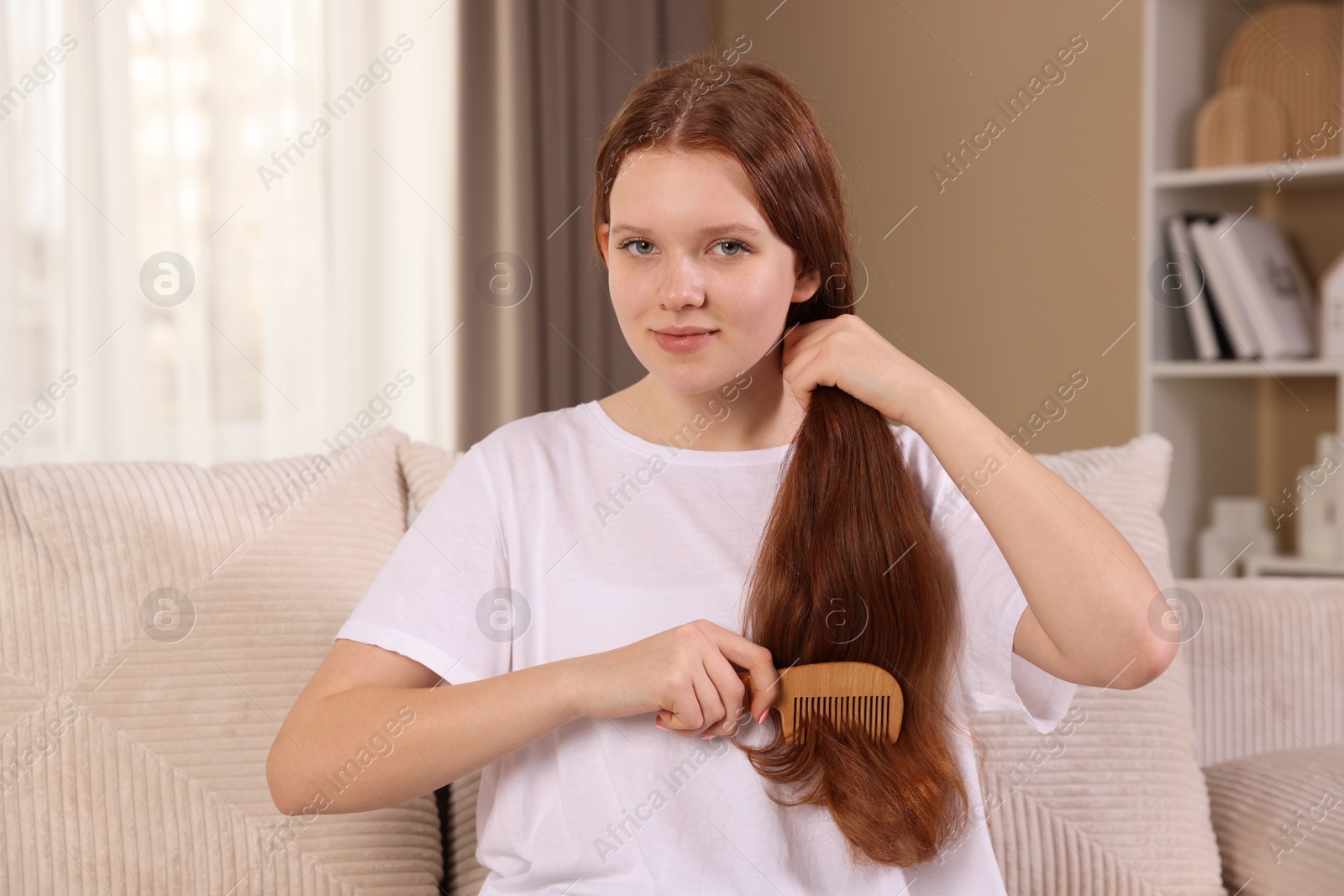 Photo of Beautiful teenage girl brushing her hair with comb at home