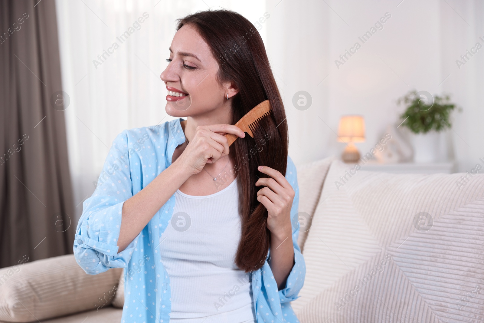 Photo of Smiling woman brushing her hair with comb at home