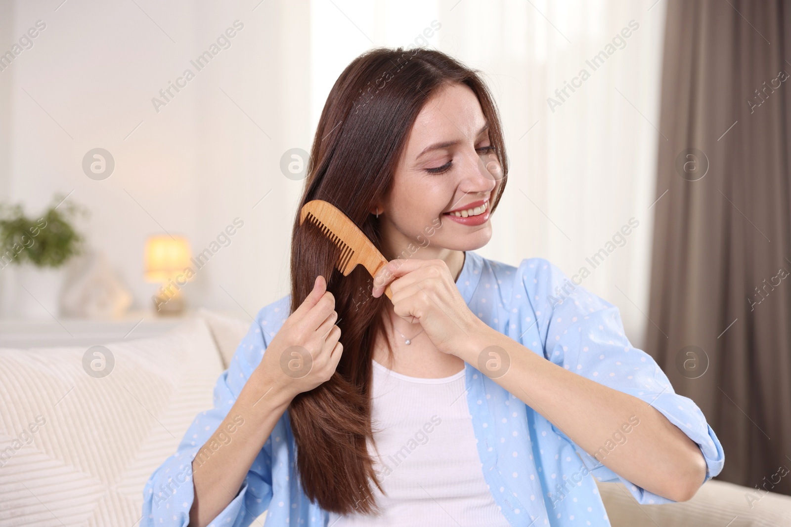 Photo of Smiling woman brushing her hair with comb at home