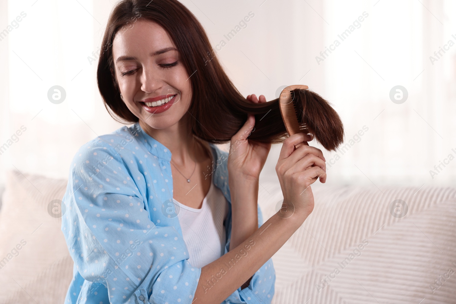 Photo of Smiling woman brushing her hair with comb at home