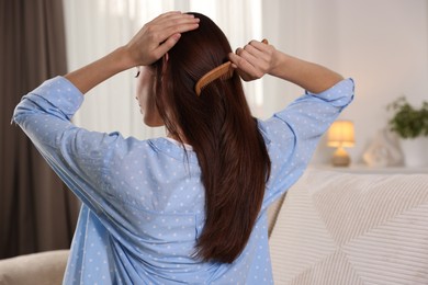 Photo of Woman brushing her hair with comb at home