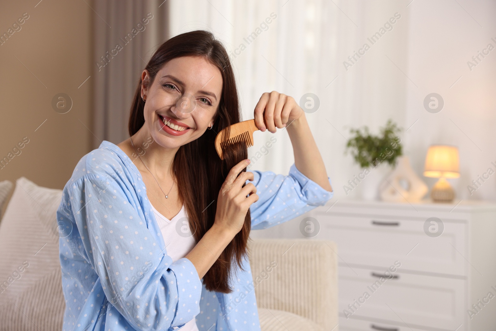 Photo of Smiling woman brushing her hair with comb at home, space for text