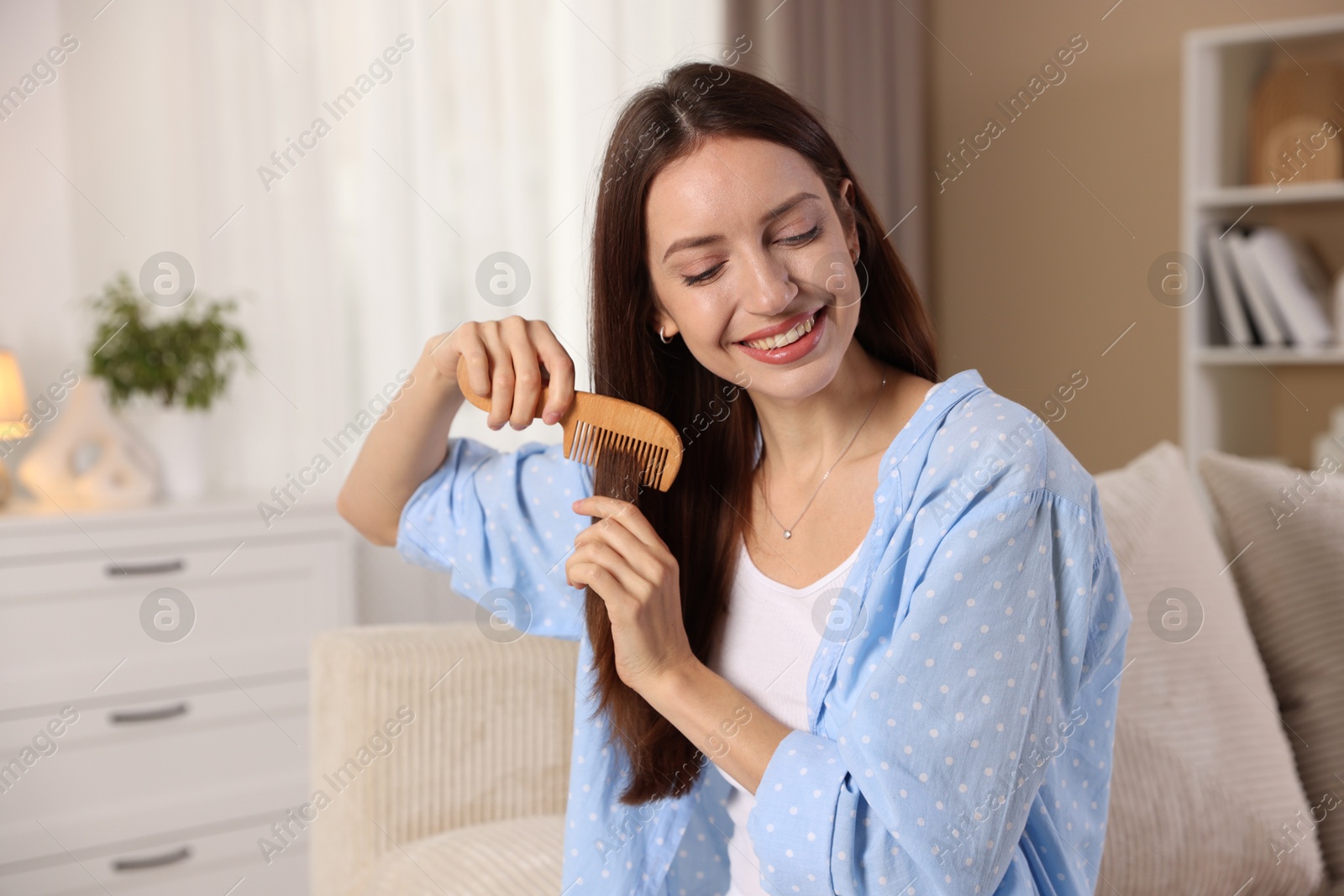 Photo of Smiling woman brushing her hair with comb at home