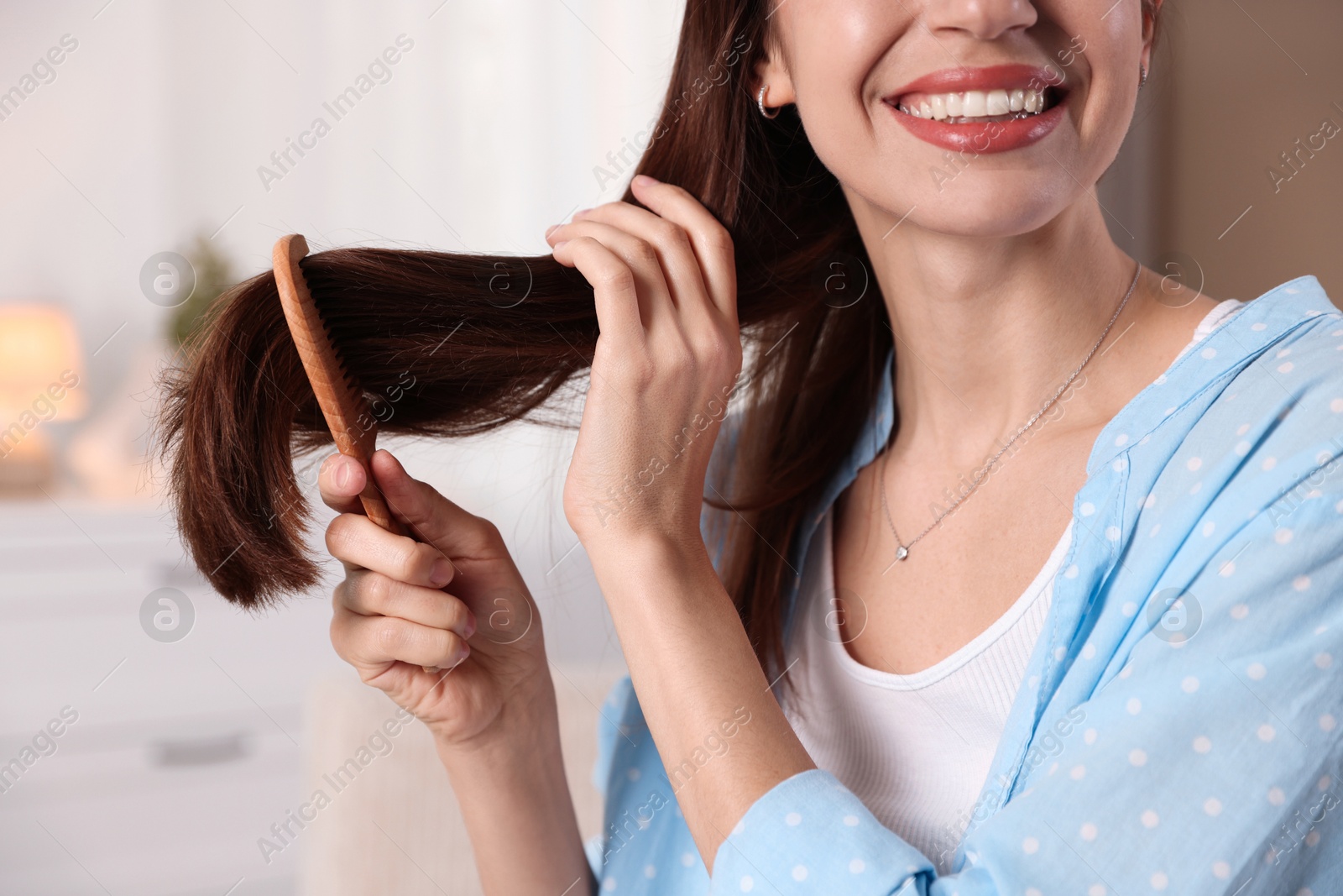 Photo of Woman brushing her hair with comb at home, closeup