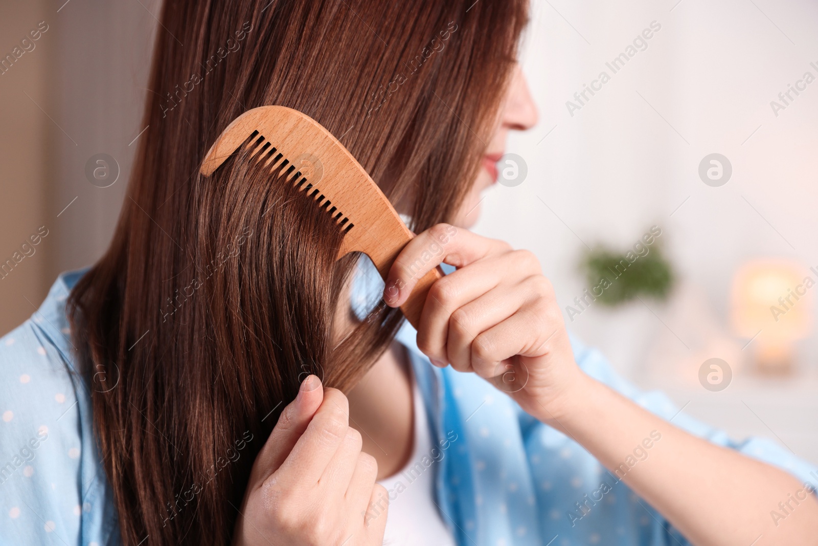 Photo of Woman brushing her hair with comb at home, closeup