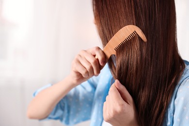 Photo of Woman brushing her hair with comb at home, closeup