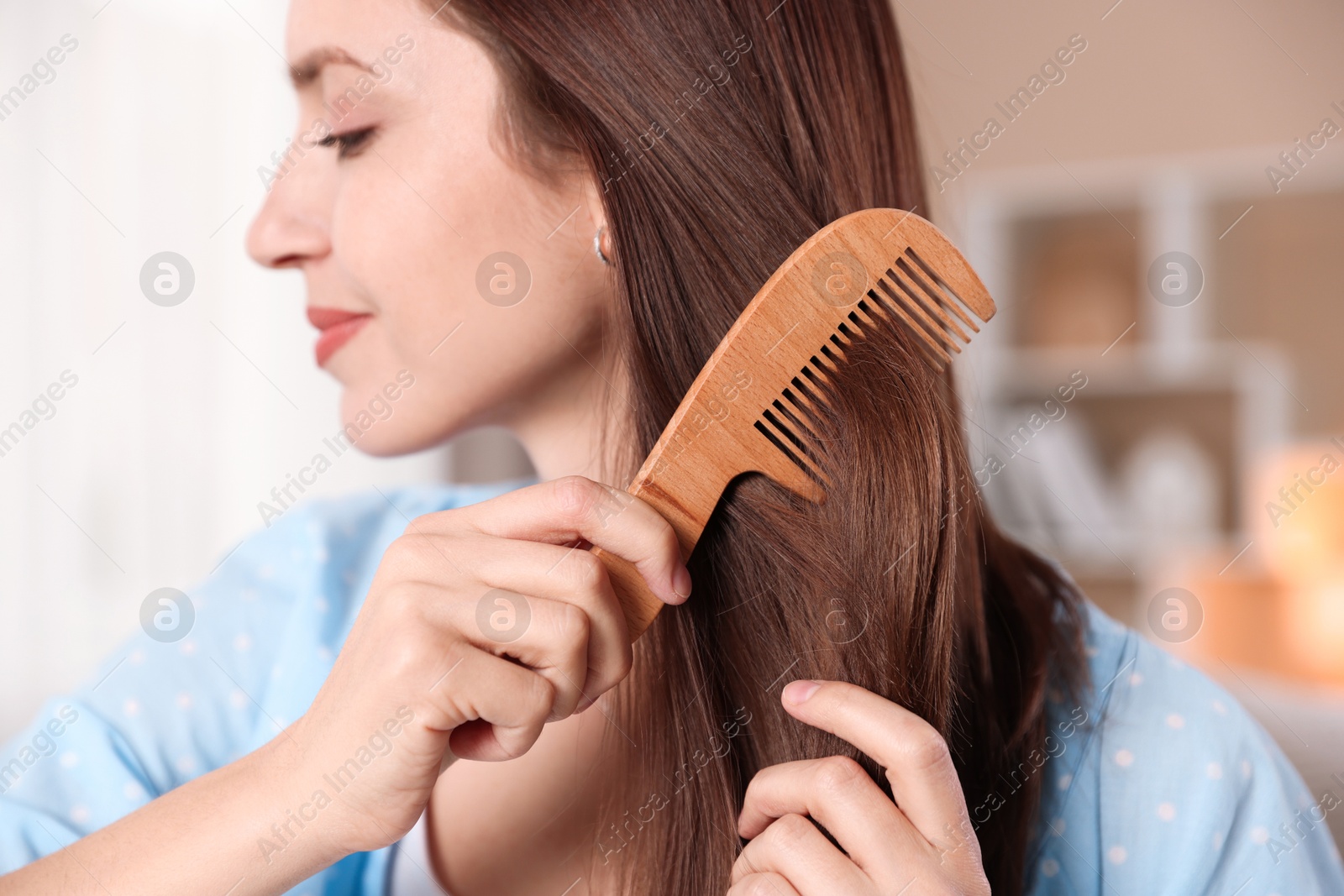 Photo of Woman brushing her hair with comb at home, selective focus