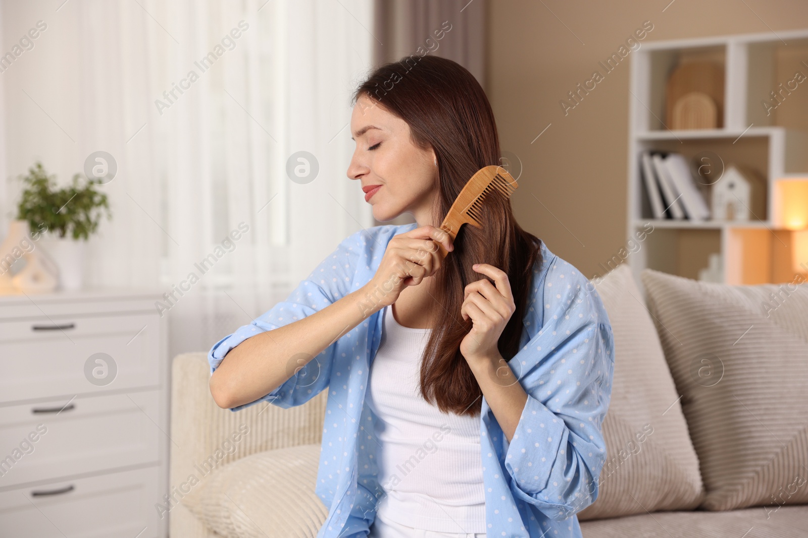 Photo of Beautiful woman brushing her hair with comb at home