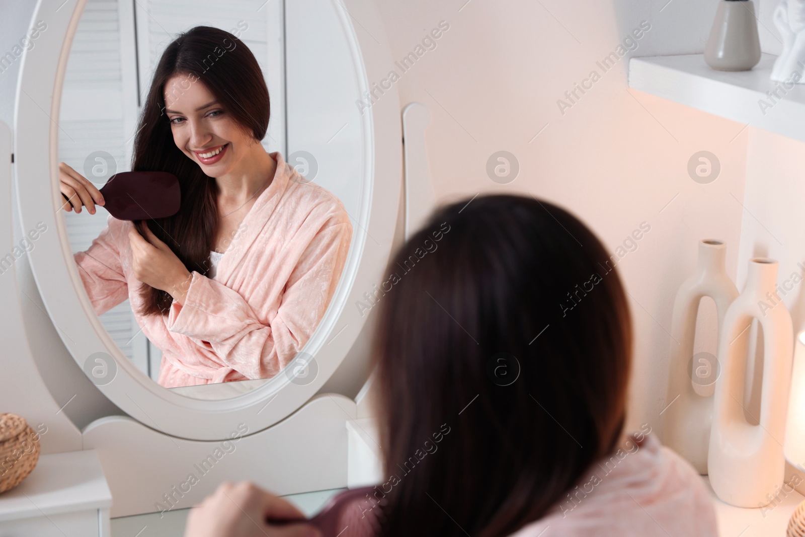 Photo of Beautiful woman brushing her hair near mirror at home, selective focus