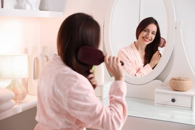 Photo of Beautiful woman brushing her hair near mirror at home, selective focus