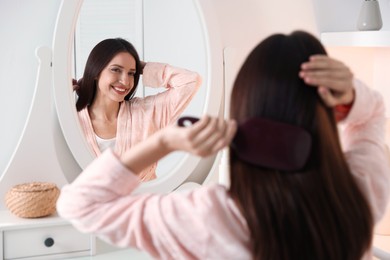 Photo of Beautiful woman brushing her hair near mirror at home, selective focus