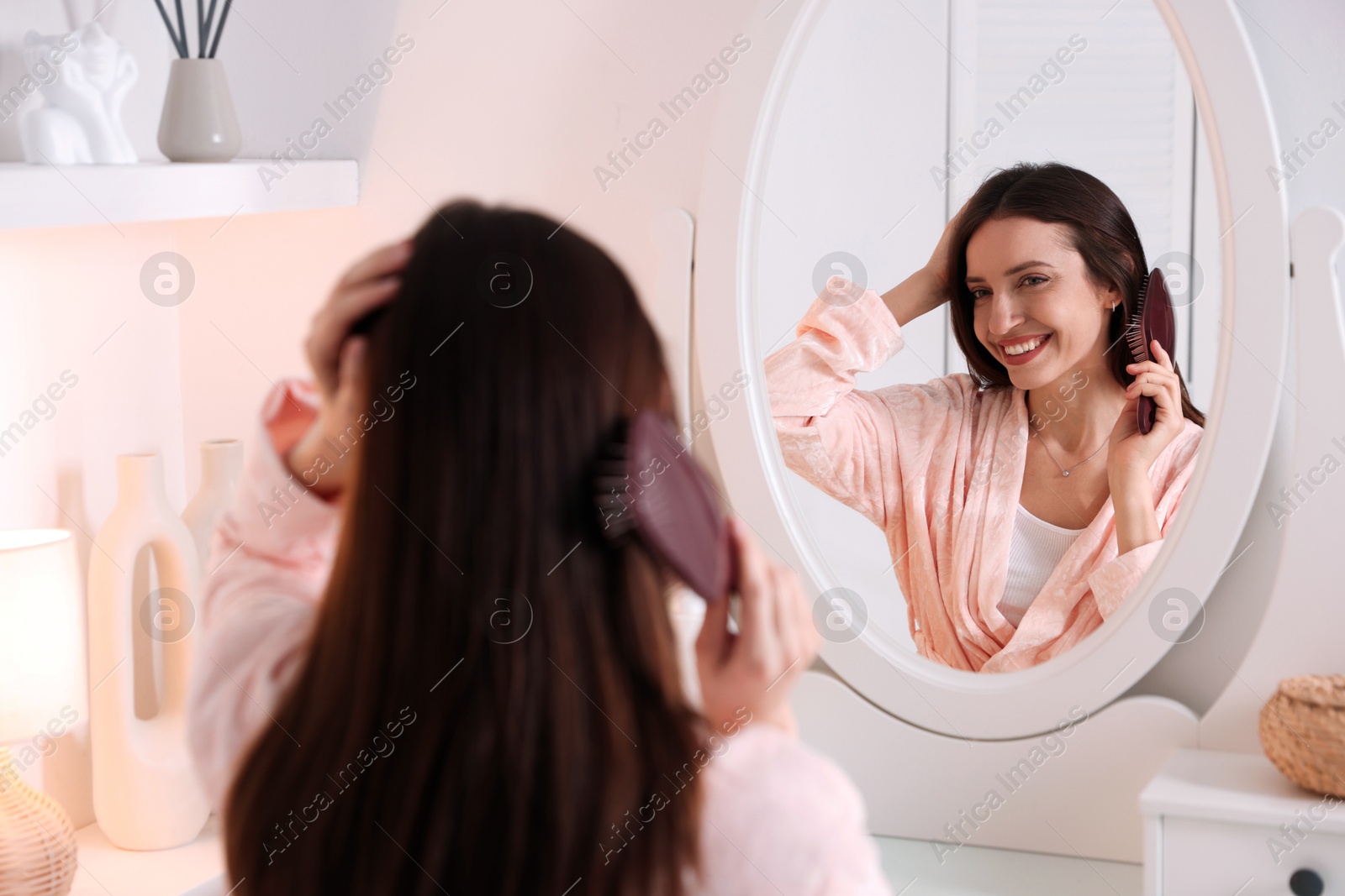 Photo of Beautiful woman brushing her hair near mirror at home, selective focus