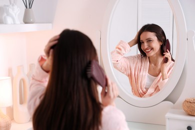 Photo of Beautiful woman brushing her hair near mirror at home, selective focus