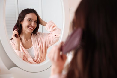 Photo of Beautiful woman brushing her hair near mirror at home, selective focus