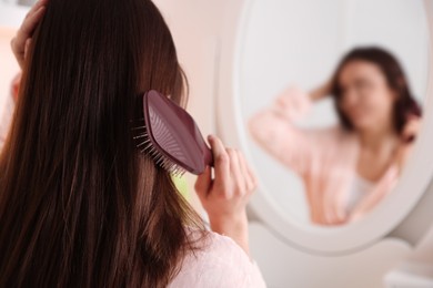 Photo of Woman brushing her hair near mirror at home, selective focus