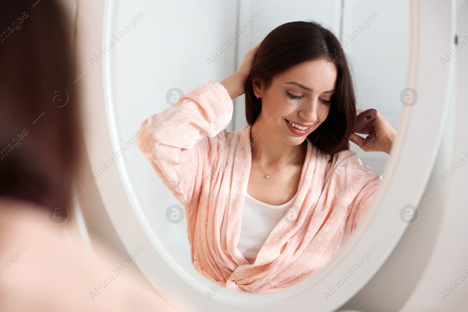 Photo of Beautiful woman brushing her hair near mirror at home, selective focus