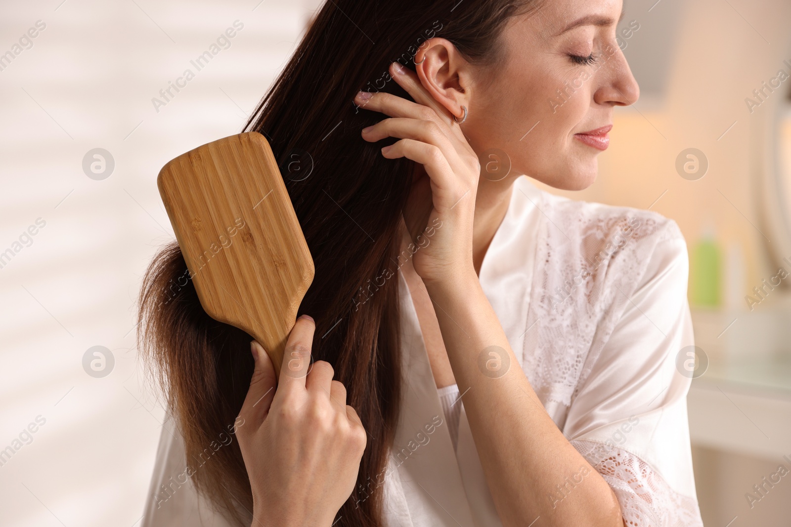 Photo of Beautiful woman brushing her hair at home, closeup