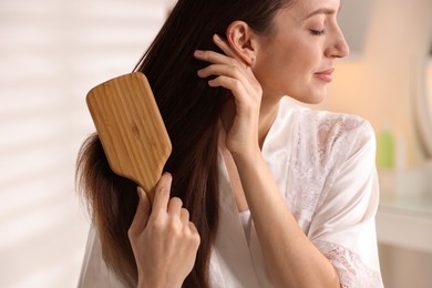 Photo of Beautiful woman brushing her hair at home, closeup