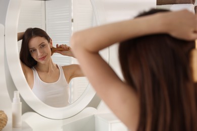 Photo of Beautiful woman brushing her hair near mirror at home, selective focus