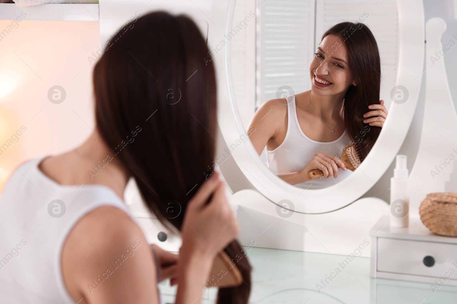 Photo of Smiling woman brushing her hair near mirror at home, selective focus