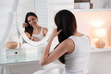 Photo of Smiling woman brushing her hair near mirror at home, selective focus