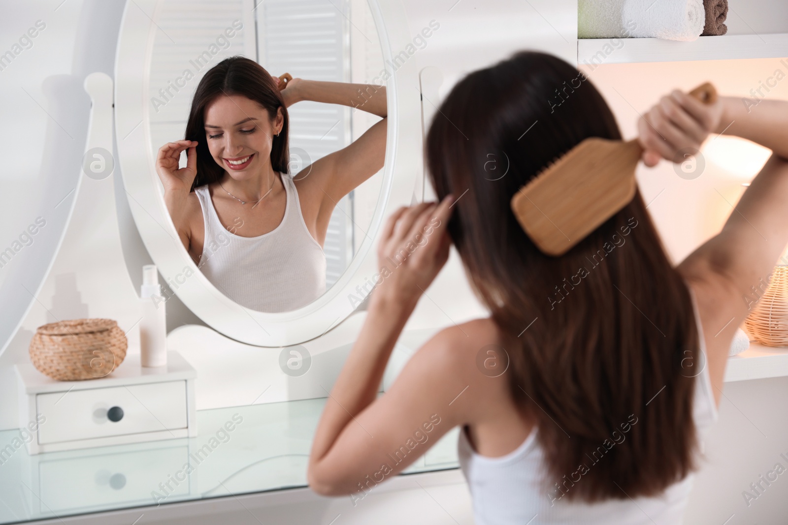 Photo of Smiling woman brushing her hair near mirror at home, selective focus