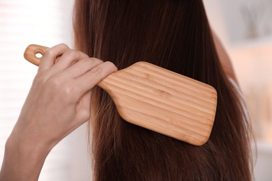 Photo of Woman brushing her beautiful hair indoors, closeup