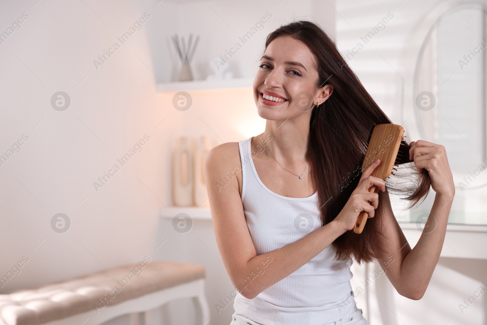 Photo of Smiling woman brushing her hair at home, space for text