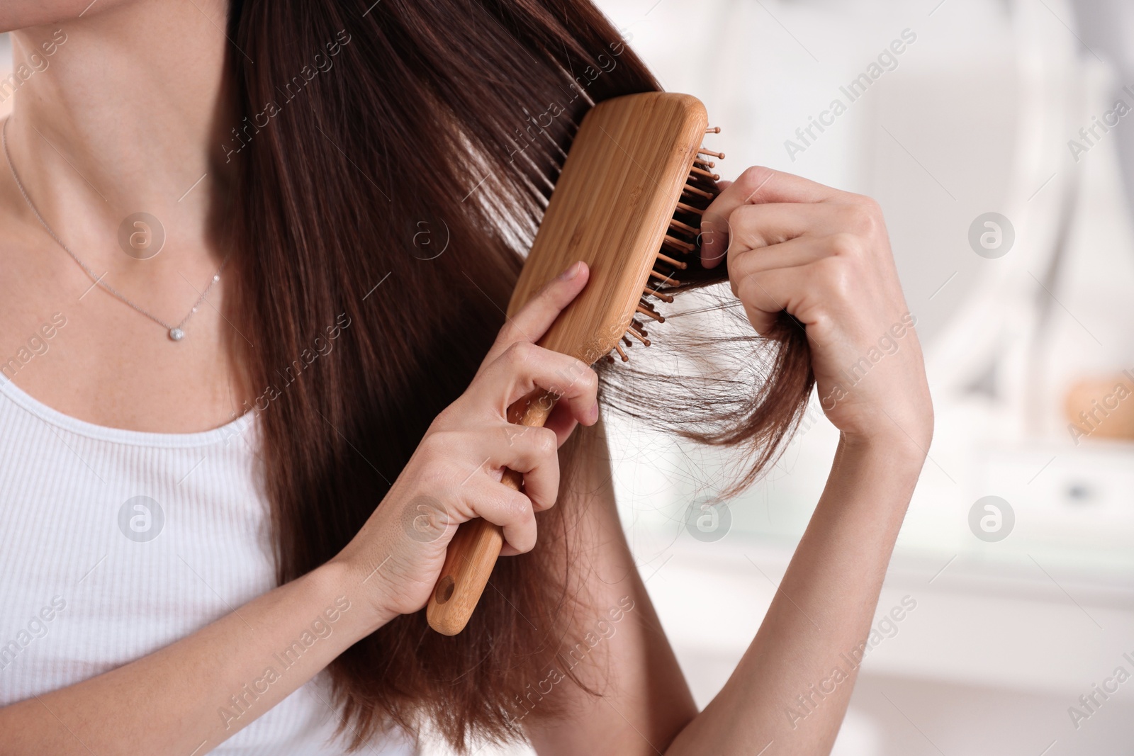 Photo of Woman brushing her beautiful hair indoors, closeup