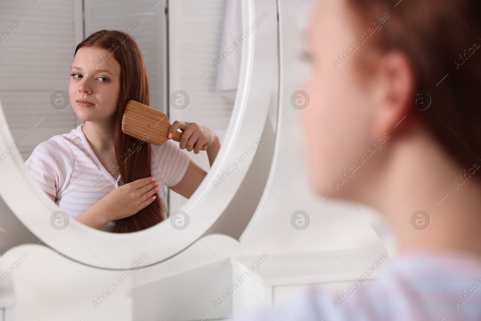 Photo of Beautiful teenage girl brushing her hair near mirror at home, selective focus