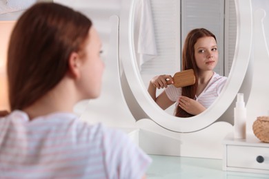 Photo of Beautiful teenage girl brushing her hair near mirror at home, selective focus