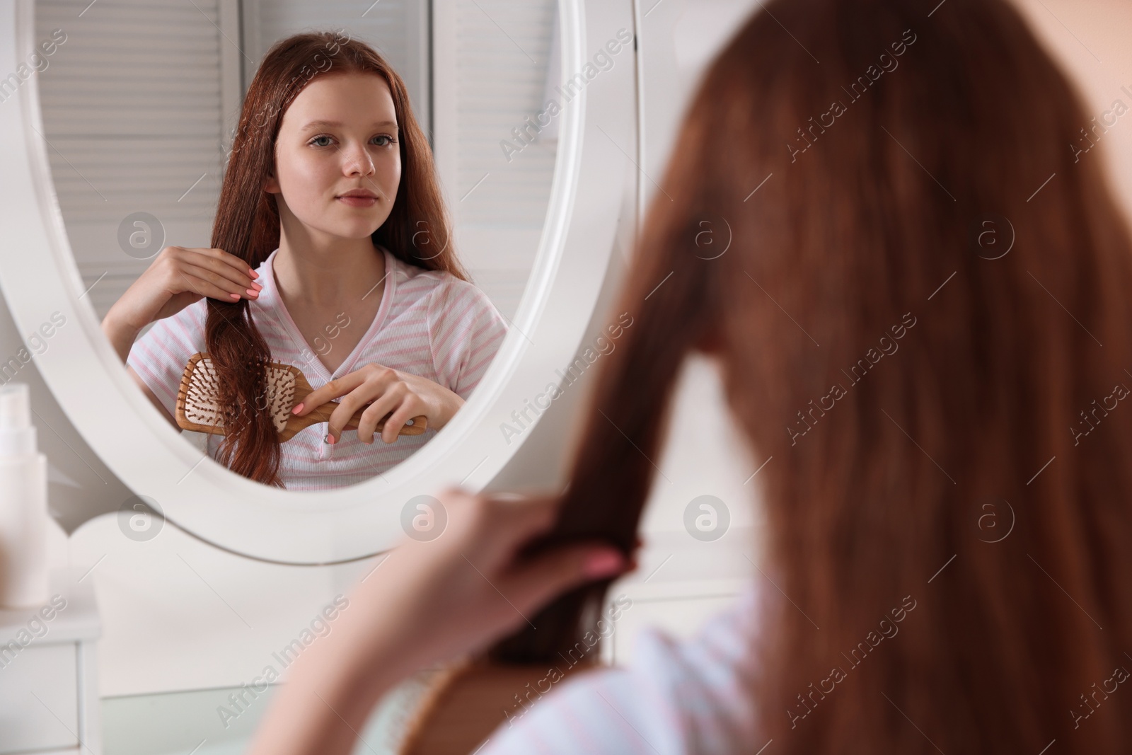 Photo of Beautiful teenage girl brushing her hair near mirror at home, selective focus