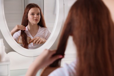 Photo of Beautiful teenage girl brushing her hair near mirror at home, selective focus