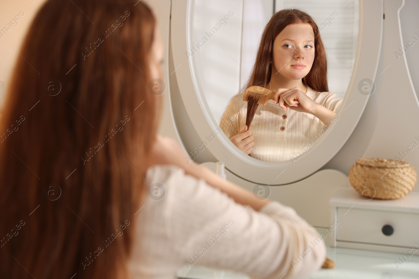 Photo of Beautiful teenage girl brushing her hair with comb near mirror at home, selective focus