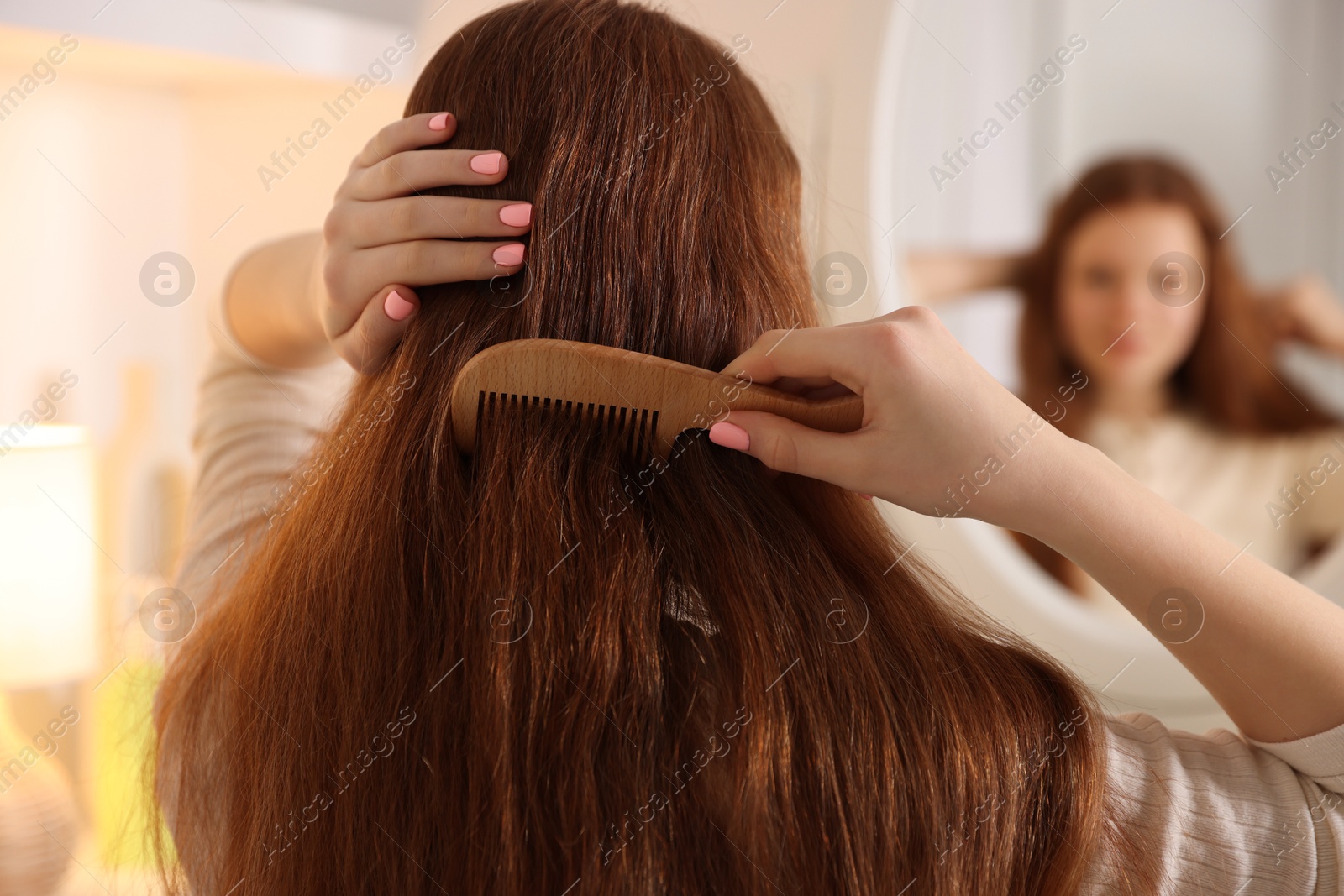 Photo of Teenage girl brushing her hair with comb near mirror at home, selective focus