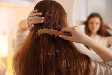 Photo of Teenage girl brushing her hair with comb near mirror at home, selective focus