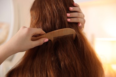 Photo of Teenage girl brushing her hair with comb at home, closeup