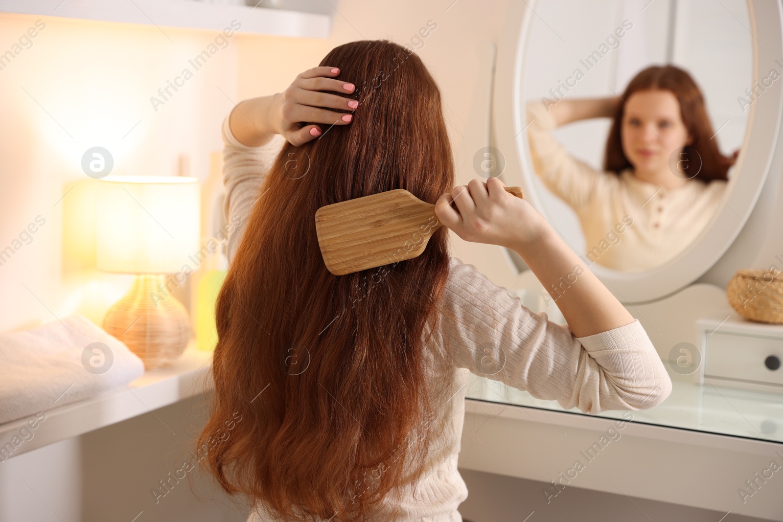 Photo of Teenage girl brushing her hair near mirror at home, selective focus