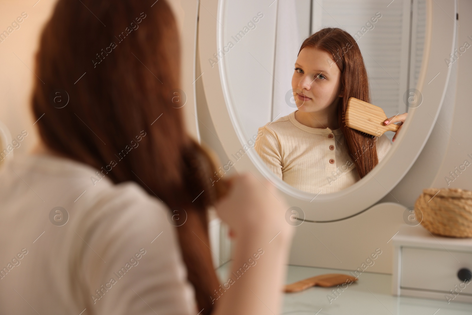 Photo of Beautiful teenage girl brushing her hair near mirror at home, selective focus