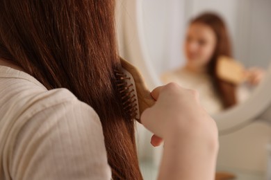 Photo of Teenage girl brushing her hair near mirror at home, closeup. Selective focus