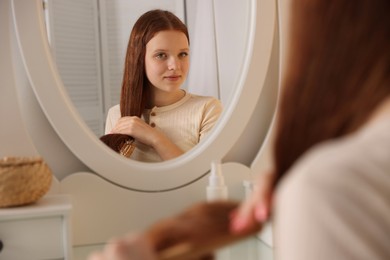 Photo of Beautiful teenage girl brushing her hair near mirror at home, selective focus