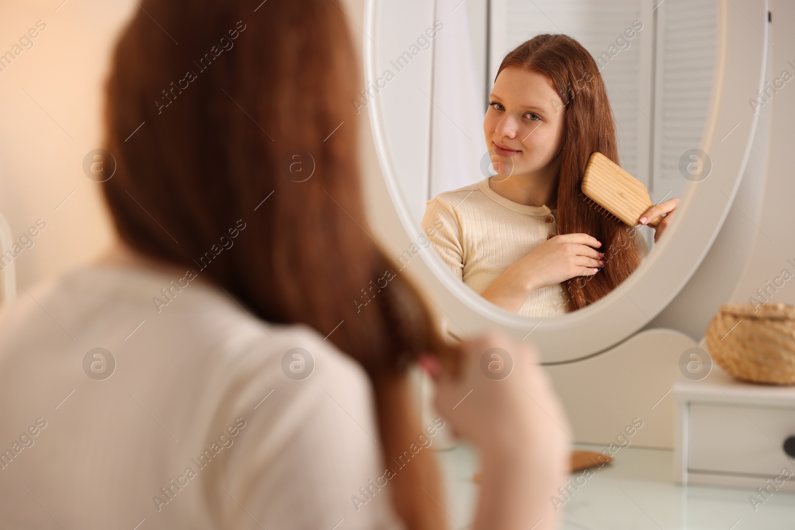 Photo of Beautiful teenage girl brushing her hair near mirror at home, selective focus