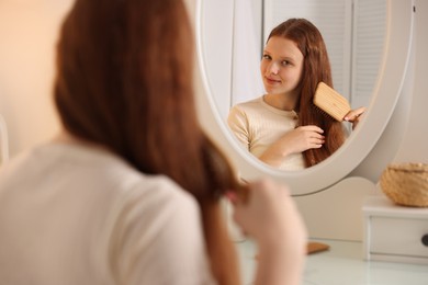 Photo of Beautiful teenage girl brushing her hair near mirror at home, selective focus