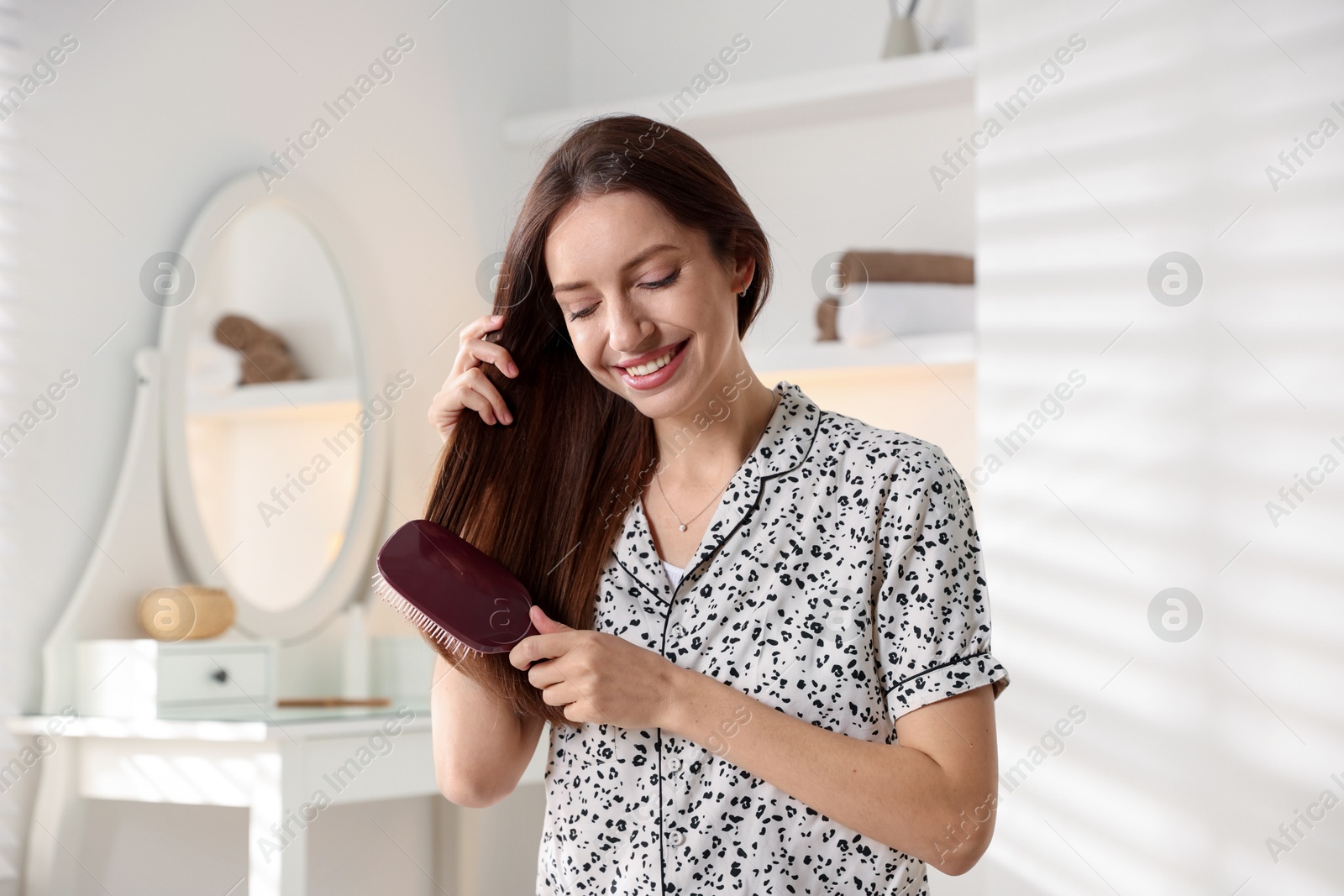 Photo of Smiling woman brushing her hair at home