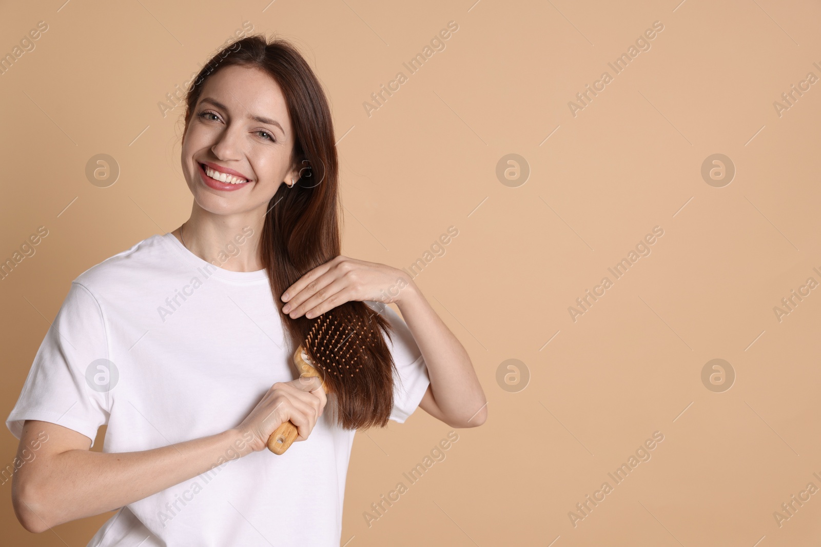 Photo of Smiling woman brushing her hair on beige background, space for text