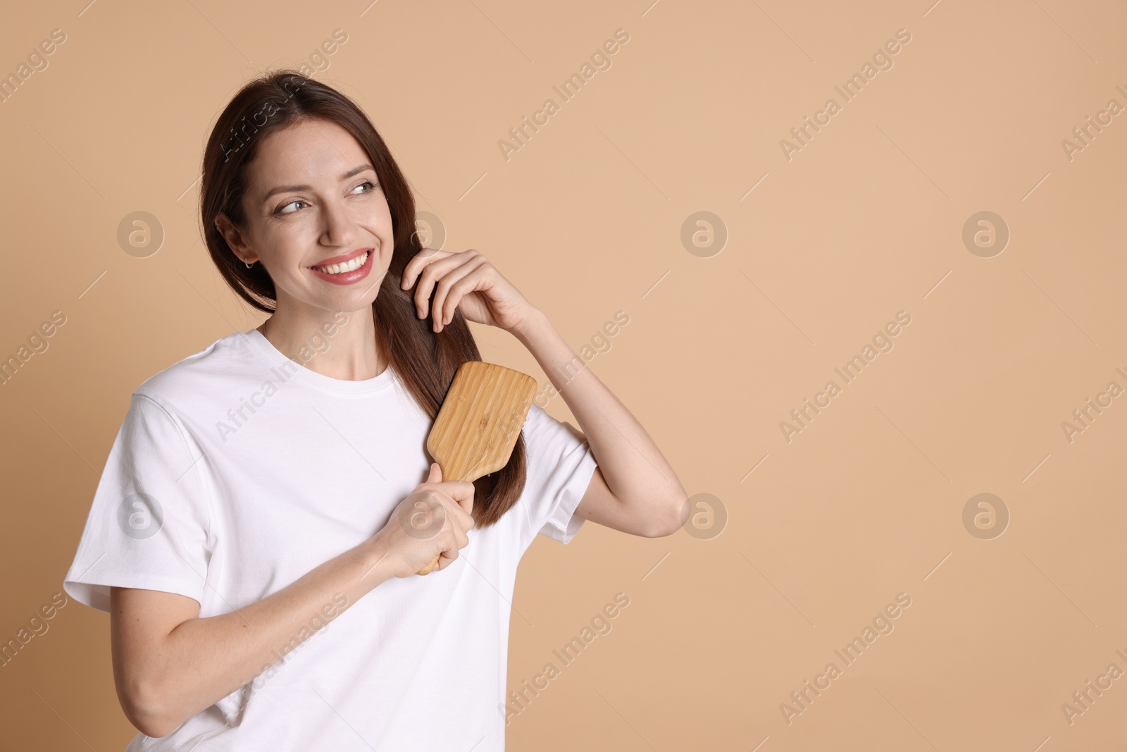 Photo of Smiling woman brushing her hair on beige background, space for text