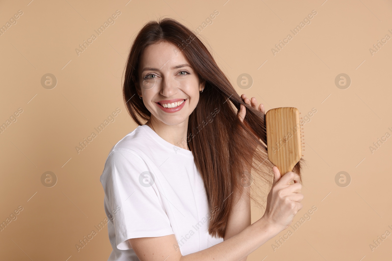 Photo of Smiling woman brushing her hair on beige background