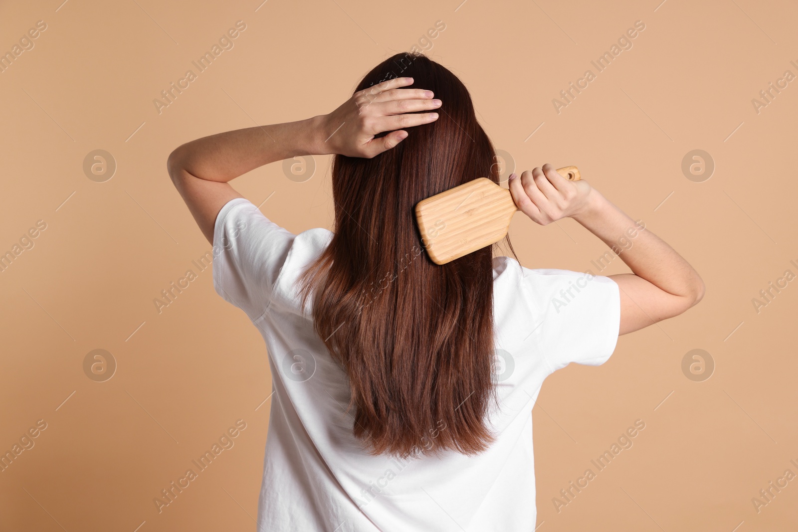 Photo of Woman brushing her hair on beige background, back view