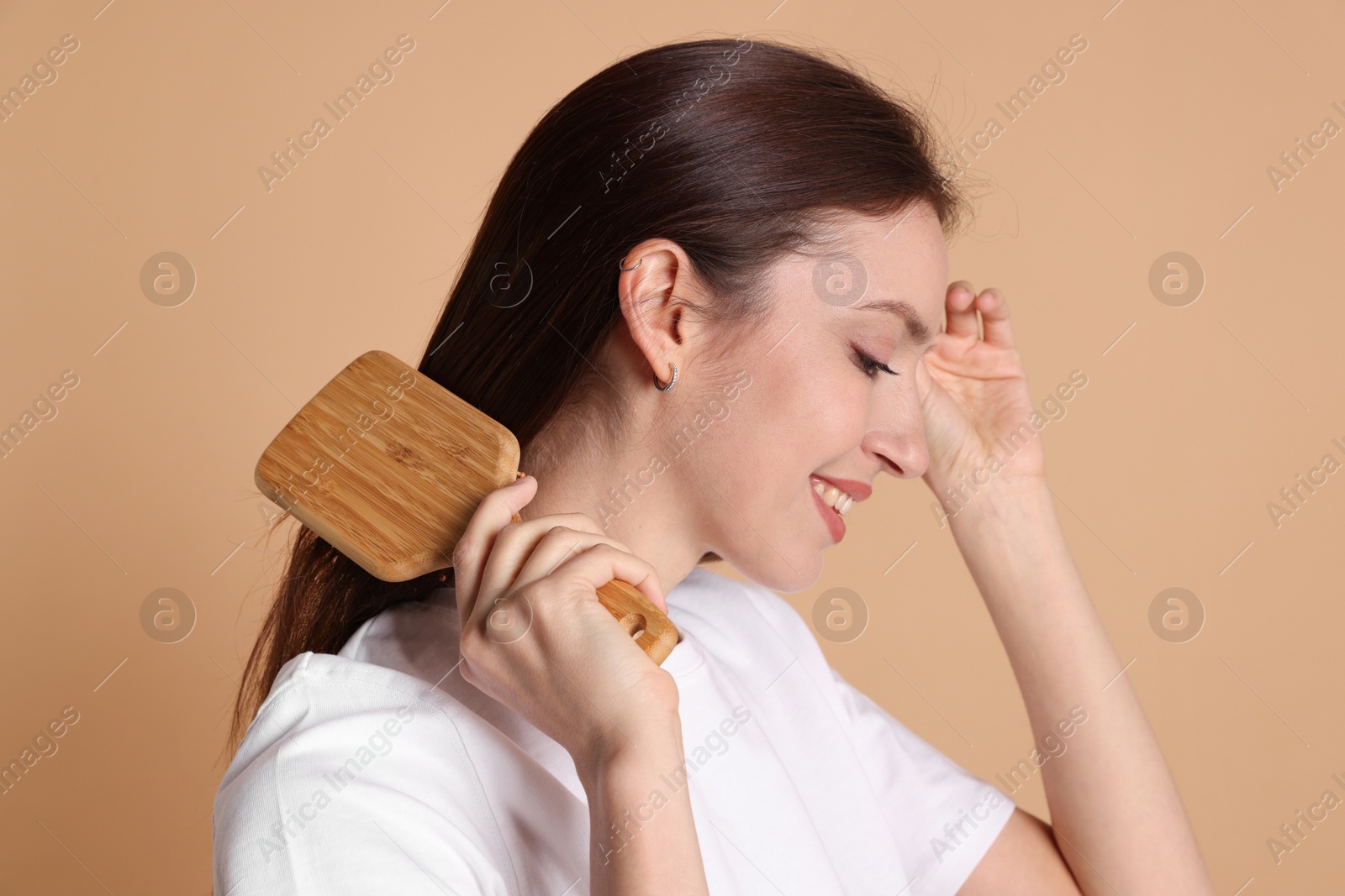 Photo of Smiling woman brushing her hair on beige background