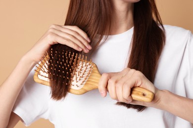 Photo of Woman brushing her hair on beige background, closeup